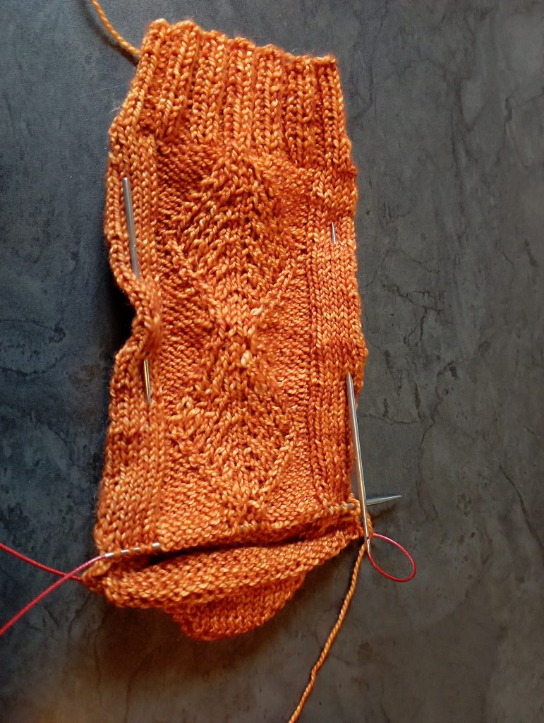 Chaussette du modèle Cordes fait main en cours de tricot : le bord côtes, la tige décorée d'un motif texturé et le talon sont déjà faits